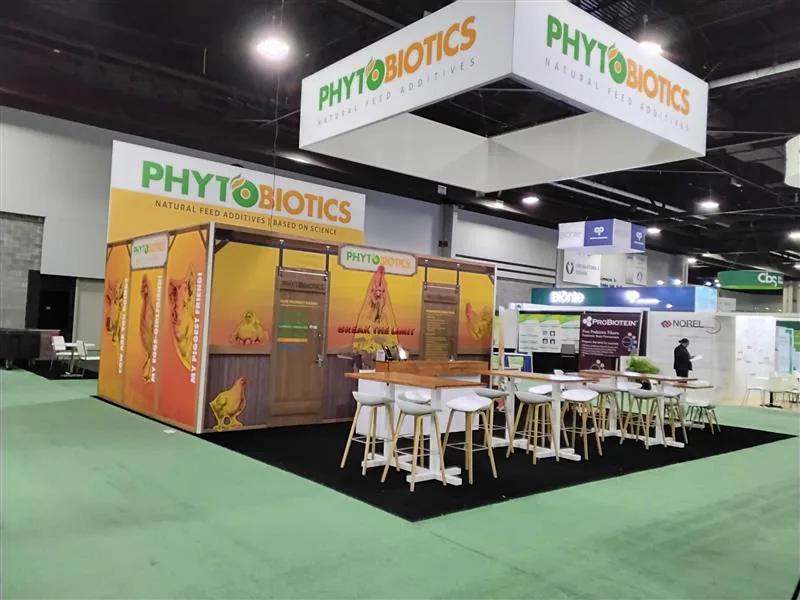Green-and-gold corner exhibit with café tables and a suspended rectangular sign.