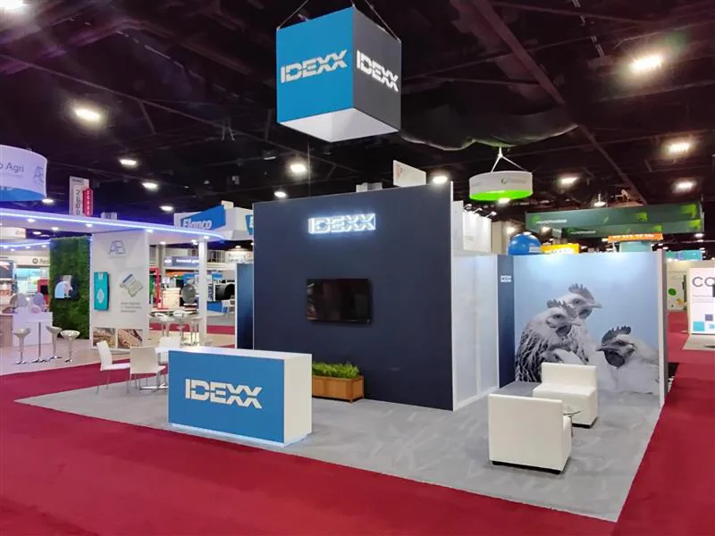 Minimal dark-blue exhibit with illuminated counters, lounge seating, and overhead cube signage.